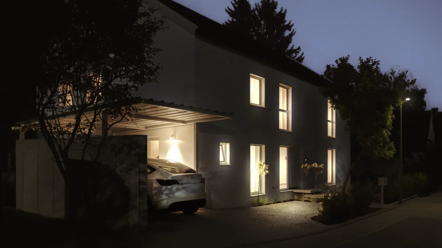 Haus bei Nacht, Blick von der Straße auf Carport und erleuchtete Fenster